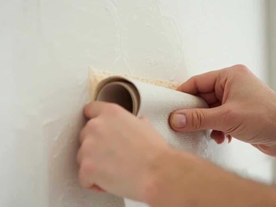 Mains appliquant du papier peint sur un mur blanc