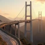 Image d'un pont suspendu enjambant un paysage montagneux sous un ciel doré au coucher du soleil