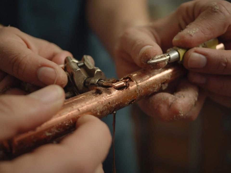 Des mains en gros plan travaillant sur un élément en cuivre à l'aide d'outils